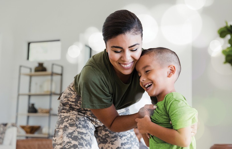Woman in camo pants hugging child and smiling.